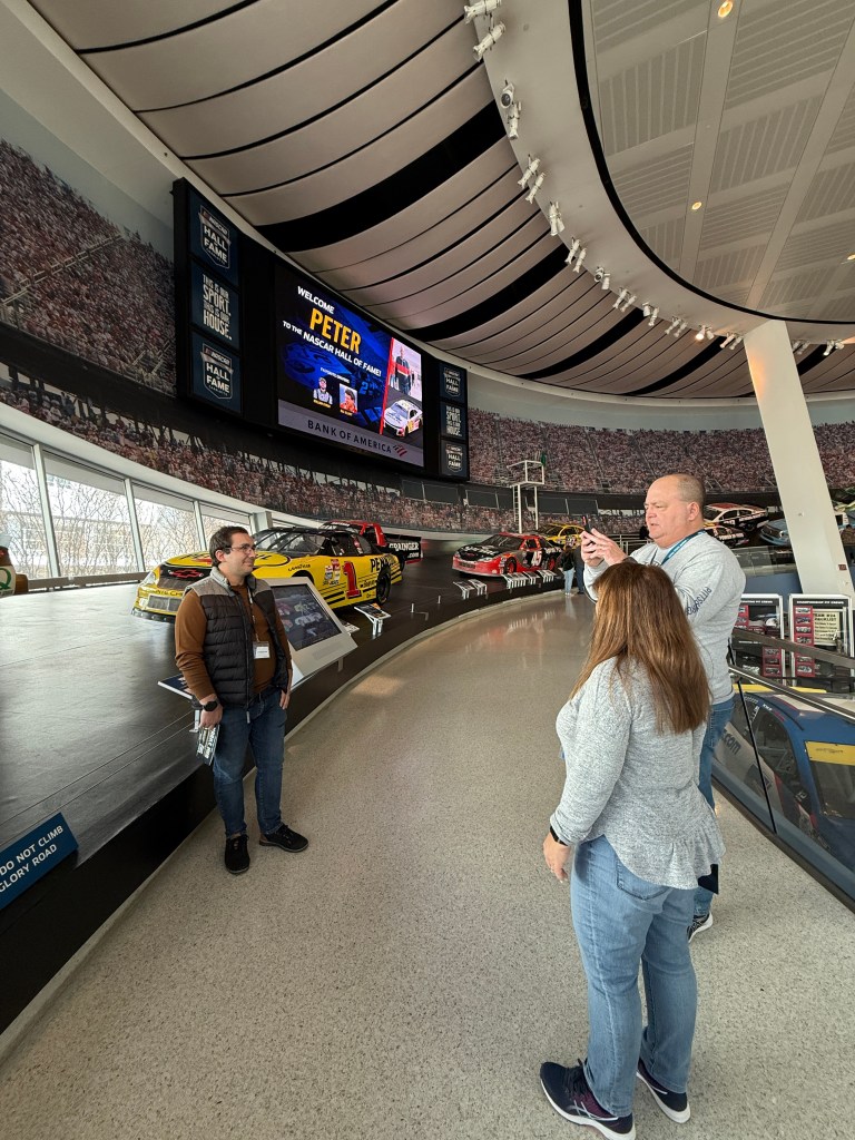 Address: 📍 400 E. Martin Luther King Jr. Blvd., Charlotte, NC 28202

It is located in Uptown (aka what Charlotte calls their downtown/ main part of the city). You will know you are in the right area when you start to see checkered sidewalks around. 

It’s easily accessible by car, with parking available at the adjacent NASCAR Plaza Parking Garage. If you’re staying in the city, you can also take the Charlotte Light Rail (the Blue line/ Lynx rail) to the Convention Center Station, which is just a short walk away. And riding the rail is less than $3 a person compared to $20+ parking in the garage. 

Admission and Pricing: 

Let's start with the current General Admission pricing for 2025: 

Adults (13-64): $27

Seniors (65+): $24

Youth (4-12): $20

Kids under 3: Free

There are two additional options as well to consider-

Combo Packages Available: If you want the full experience, look for ticket packages that include simulator rides and guided tours.

Memberships: If you're a die-hard NASCAR fan, consider a membership for unlimited entry and exclusive perks. My father in law decided to sign my husband and I up for the membership so I will update this to see if we actually go back! We were told there is events for members only so maybe we will check one of those out! 

Keep an eye out on their website as well for special promos and group rates. 

When is the best time to visit? 

Weekdays: If you want to avoid crowds, visiting on a weekday (especially in the morning) is your best bet.

Be Prepared For Race Season: Visiting during race weeks or before major NASCAR events can add extra excitement, but expect larger crowds. Definitely depends on if you like that energy or would prefer a calmer experience if you want to go during race weeks or not. 

Off-Peak Seasons: January through March tends to be quieter, making it a great time to explore at your own pace.

Charlotte event schedule: if there is things pulling in a lot of people from out of town (ie a panthers game) the hall of fame will be busier but if its a weekend with a lot just for locals (like concerts) it will be less busy. 

Must-See Exhibits & Attractions

The NASCAR Hall of Fame isn’t just about plaques and trophies—it’s a fully interactive experience. Here are some highlights you won’t want to miss:

Hall of Honor

The heart of the museum, this exhibit pays tribute to NASCAR’s greatest legends with their stories, memorabilia, and career highlights. When we went there was an incredible exhibit about the first woman to race in a NASCAR race! But take the time to look at the contributions of everyone here not just the racers! 

In the hall of honor there is also a cool set-up of video displays about each honoree with attached phones you can pick up to listen to the video. That way everyone can listen to the stories they want to hear about without it being super loud in there! Such a smart setup. 

Glory Road

A fan-favorite, this is a ramp that showcases a rotating lineup of historic NASCAR cars, complete with real-life track angles that let you experience what drivers see on the curves.

There is also a bunch of different pieces from tracks throughout that you can feel them which I personally found to be super fun but make sure to bring hand sanitizer- theres is a lot of people touching them!

High-Octane Theater

This theater runs an "action packed" summary to get you hyped before touring the museum/hall of fame. Personally skipped it but it also looked like a great place to give the kiddos a breather! 

Race Week Experience

This hands-on exhibit lets you step into the world of NASCAR teams, experiencing the prep work, pit stops, and high-pressure decision-making that goes into every race.

iRacing Simulator

Ever wondered what it’s like to be behind the wheel of a NASCAR stock car? The iRacing simulator lets you experience it first-hand, racing against other visitors in a virtual track setting. 

This was a BLAST though definitely listen and do the practice simulators on the yellow wall (go the opposite direction to the furthest wall from the simulators on the same level). We skipped and honestly it made it so much harder! 

Pit Crew Challenge

Put your speed and coordination to the test in a timed pit stop challenge where you change a tire just like a real NASCAR crew member. If you have enough people you can also compete with people in your group for who can finish faster. Proud to say my husband and I won lol!

How Long to Spend at the NASCAR Hall of Fame

Average Visit Time: 2-3 hours

If you're a casual fan, 2-3 hours is plenty to explore the exhibits, try out a few interactive stations, and soak in the experience. Hardcore NASCAR enthusiasts might want to dedicate 4+ hours to read through all the detailed history and try every simulator.

Bonus tips for a fun visit: 

✔️ Wear Comfortable Shoes – There’s a lot of walking, especially on the banked “Glory Road” exhibit.
✔️ Bring a Camera – Plenty of cool photo ops with legendary cars and interactive exhibits.
✔️ Go Early or Late – Arriving right when they open or a couple of hours before closing helps you avoid crowds.
✔️ Check the Calendar – Look for special events, meet-and-greets, or racing simulations that might be happening during your visit.